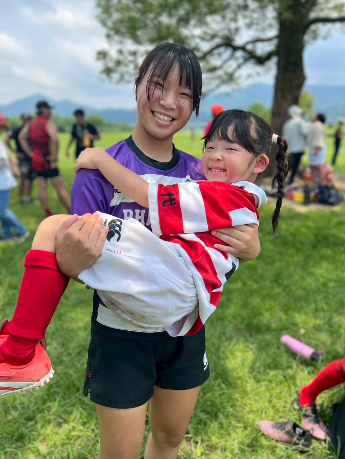 学生ラガールに抱き上げられ笑顔を見せる幼児ラガール。ラグビーファミリーの温かい絆が育まれている。