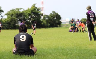 グラウンドでラグビー練習を見守る中学生選手の後ろ姿。