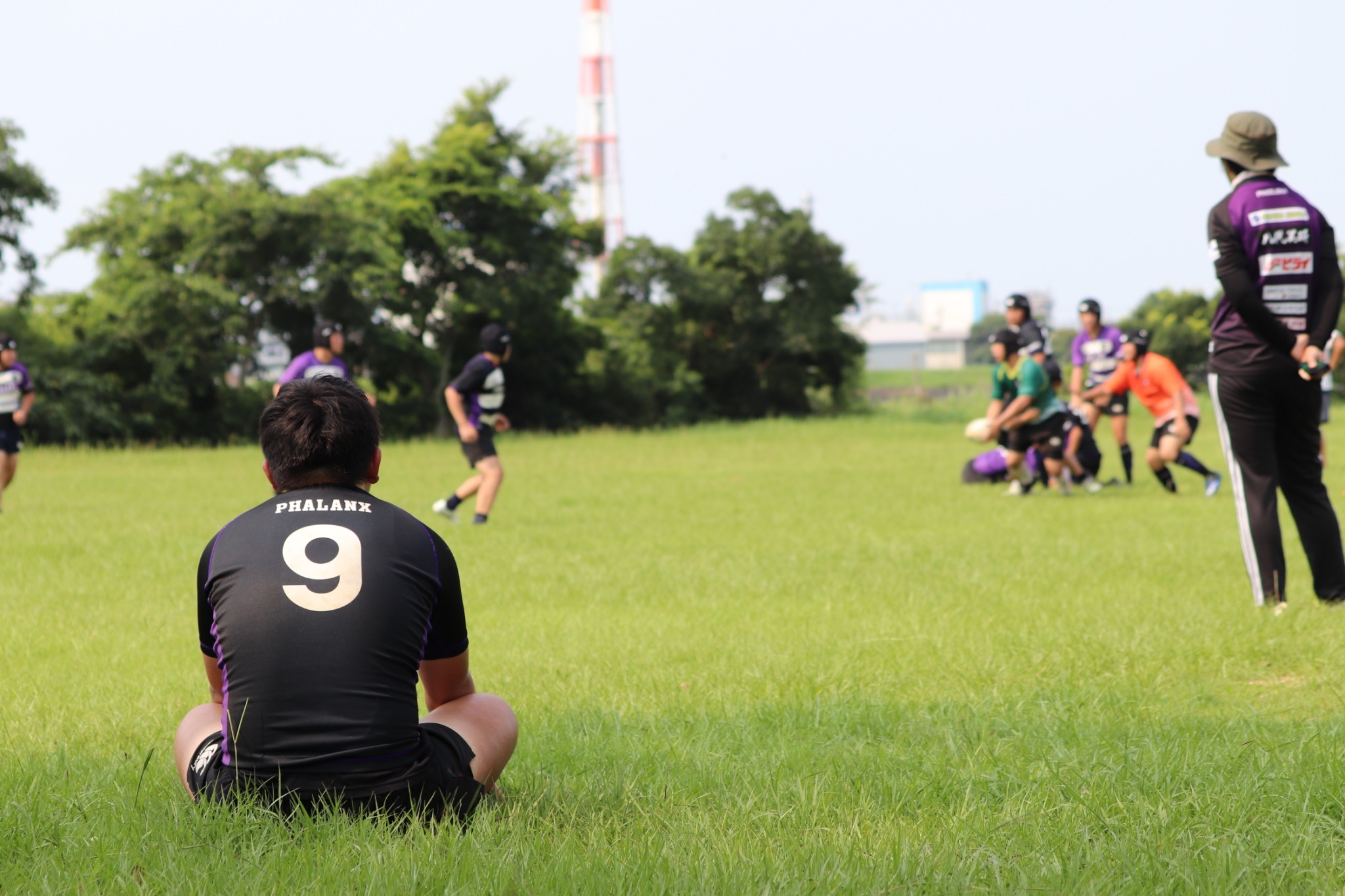 グラウンドでラグビー練習を見守る中学生選手の後ろ姿。